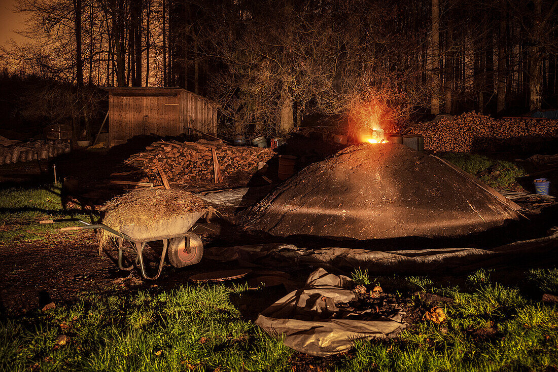 lit kiln with wheelbarrow and straw in front at night, charcoal production, Aalen, Baden-Wuerttemberg, Germany