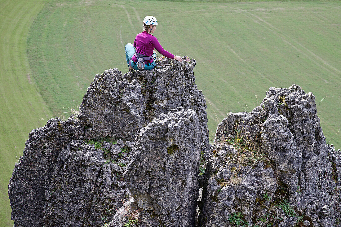Young female climber sitting on the top of a high rock, Pottenstein, Franconia, Germany