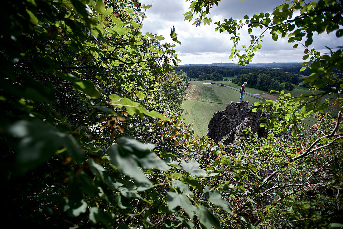 Junge Kletterin steht auf der Spitze eines hohen Felsens, Pottenstein, Franken, Deutschland