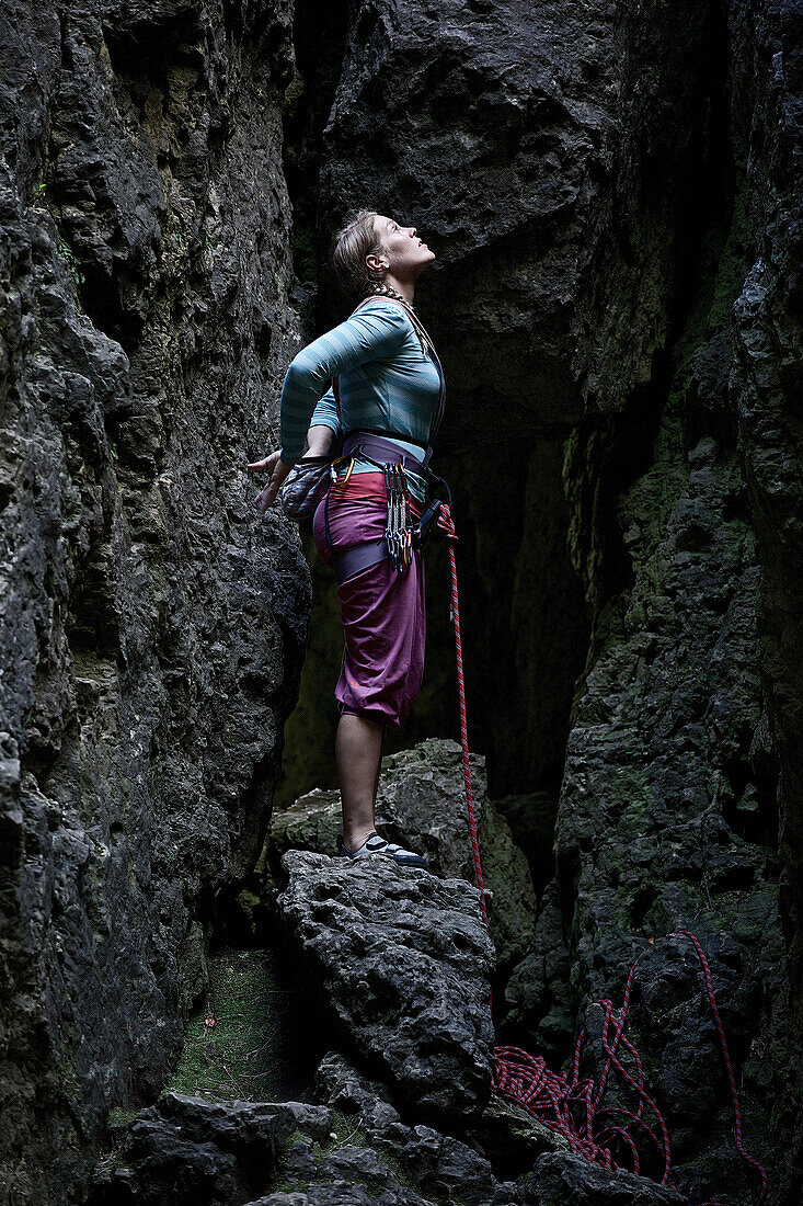 Young female climber standing between rocks and looking up, Pottenstein, Franconia, Germany
