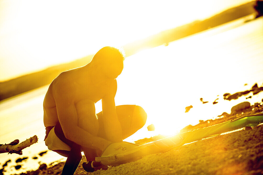 Young male windsurfer rigging up his sail on a sunny evening, Ammersee, Bavaria, Germany