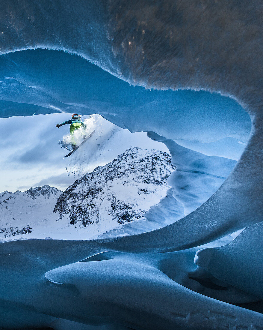 Young male snowboarder jumping down from a cave of a glacier, Pitztal, Tyrol, Austria