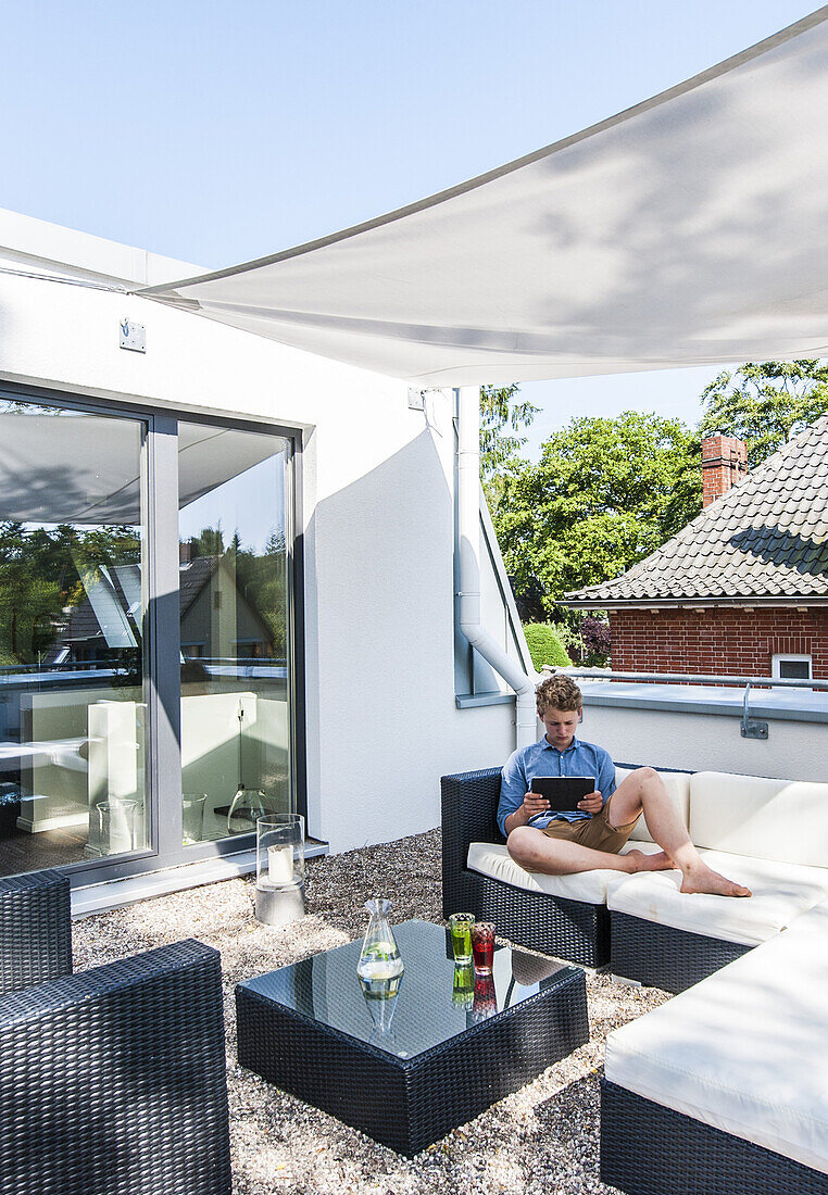young guy with iPad on the roof top of a modern sigle-family house in Hamburg, north Germany, Germany