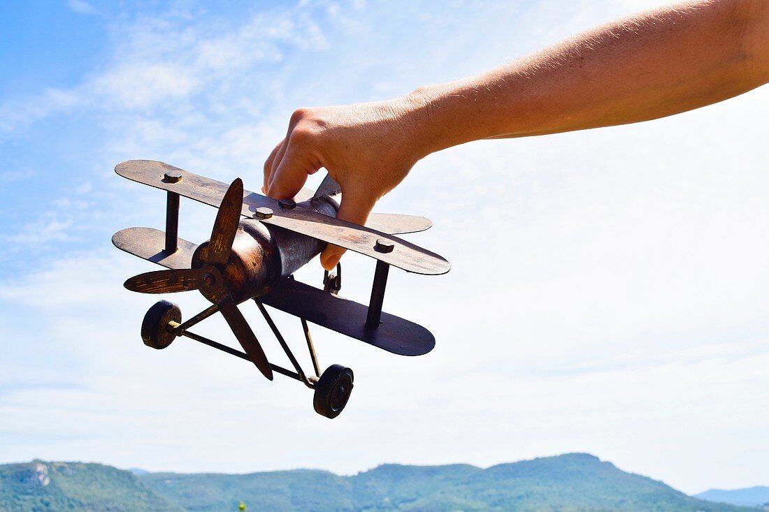 Close-up of  hand holding a model airplane against sky and mountain range.
