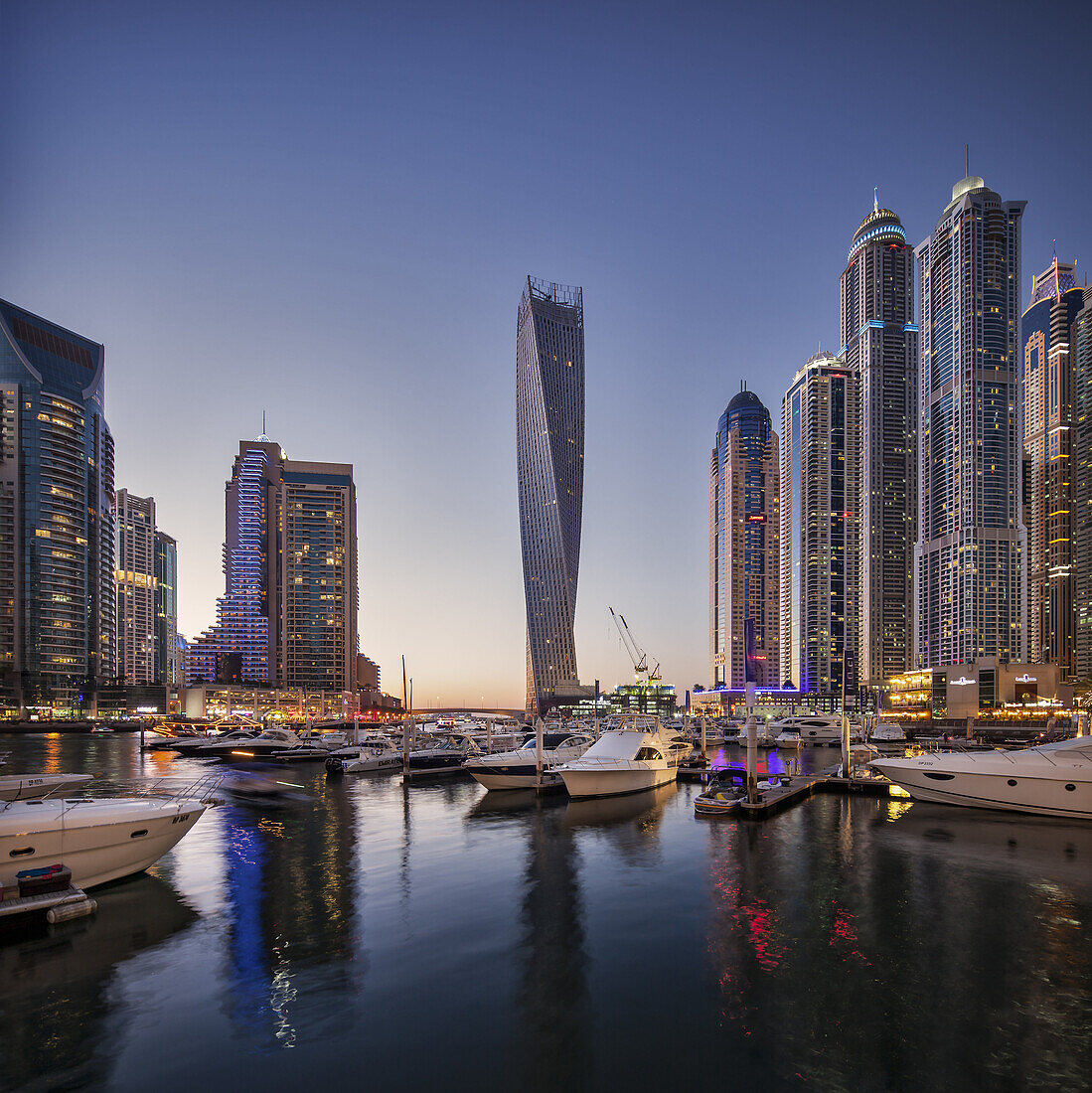 Dubai Marina at twilight with the Cayan Tower (Infinity Tower), the Dubai Marriott Harbour Hotel and Suites and various residential towers, Dubai Marina, Dubai, The United Arab Emirates.