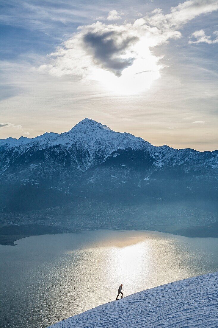 Hiker admires Lake Como and Mount Legnone on a cold winter morning Vercana mountains High Lario Lombardy Italy Europe.