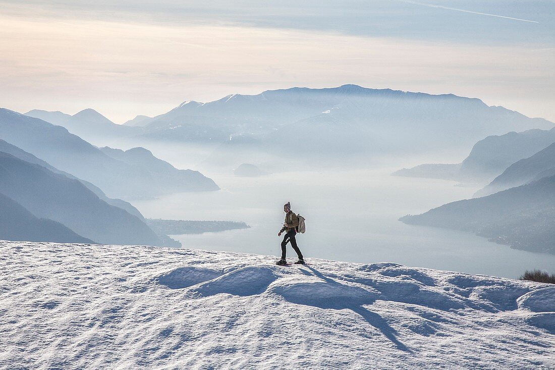 Winter view of Lake Como while a hiker proceeds with snowshoes Vercana mountains High Lario Lombardy Italy Europe.