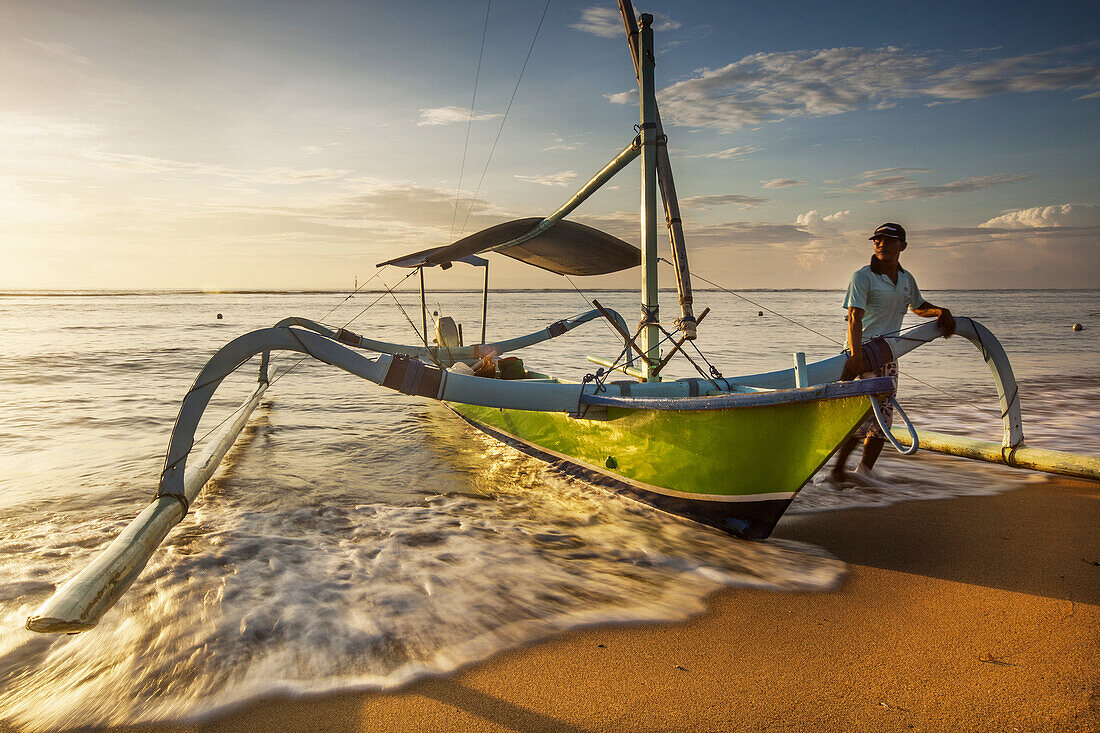Fishing vessel with outriggers on beach at dawn, Sanur, Bali, Indonesia.