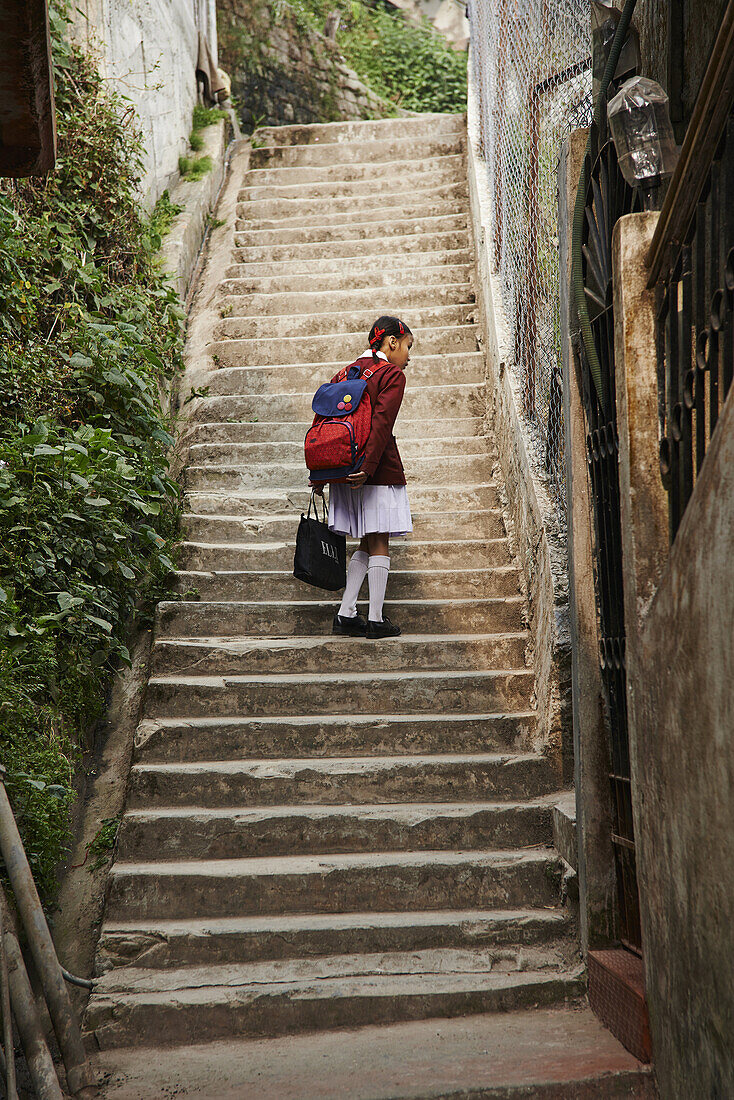 A young school girl walking up the stairs curious looks at something on the wall in the back streets of Darjeeling.