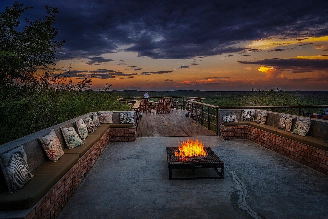 Campfire and woman enjoying the sunset, Etosha Safari Lodge, Etosha National Park, Namibia, Africa.