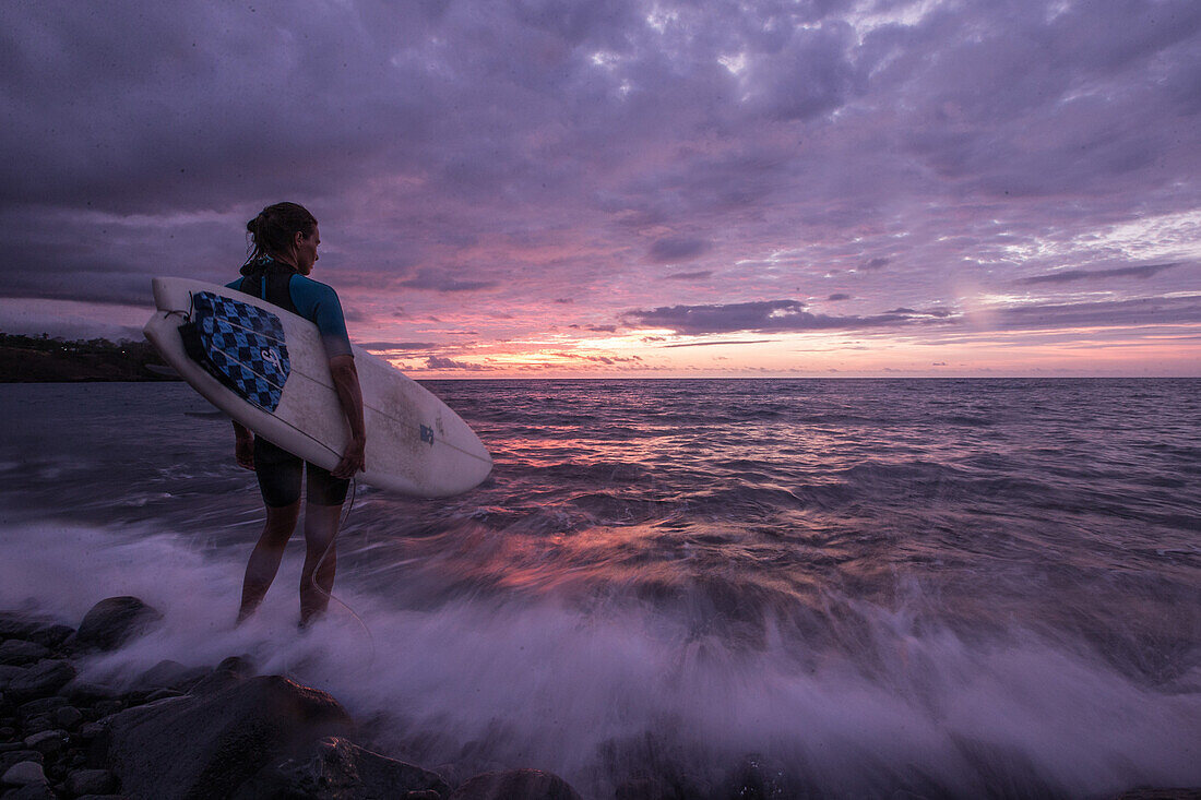 Young female surfer standing in front of the sea at sunset, Sao Tome, Sao Tome and Principe, Africa