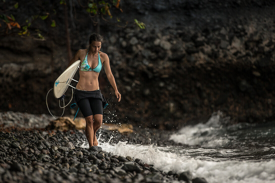 Young female surfer walking along the beach with her surfboard, Sao Tome, Sao Tome and Príncipe, Africa