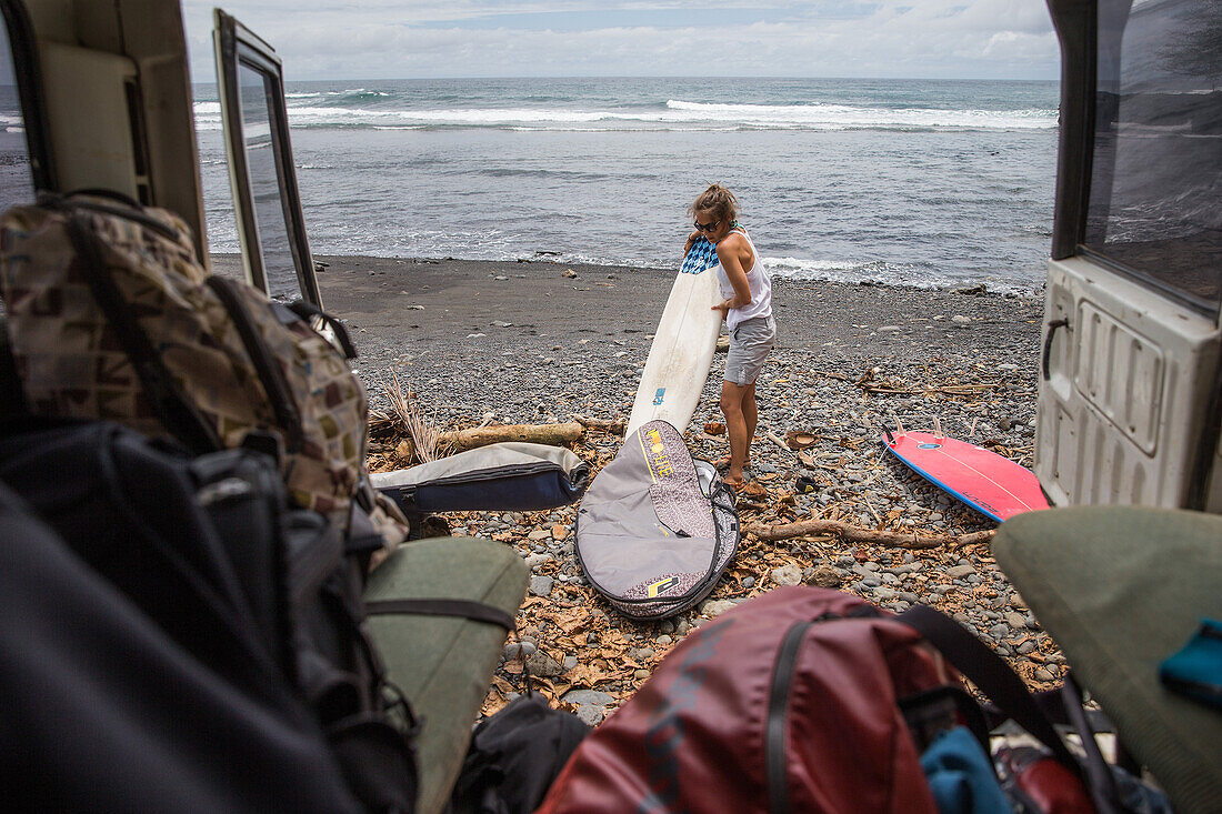 Junge Surferin nimmt ihr Surfbrett aus einer Tasche am Strand, Sao Tome, Sao Tome und Príncipe, Afrika