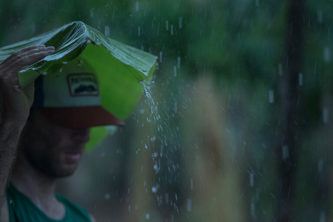 Junge Mann hält ein großes Blatt über seinen Kopf um sich vor dem Regen zu schützen, Sao Tome, Sao Tome und Príncipe, Afrika