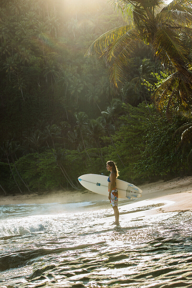 Junge Surferin steht am Strand mit ihrem Surfbrett, Sao Tome, Sao Tome und Príncipe, Afrika