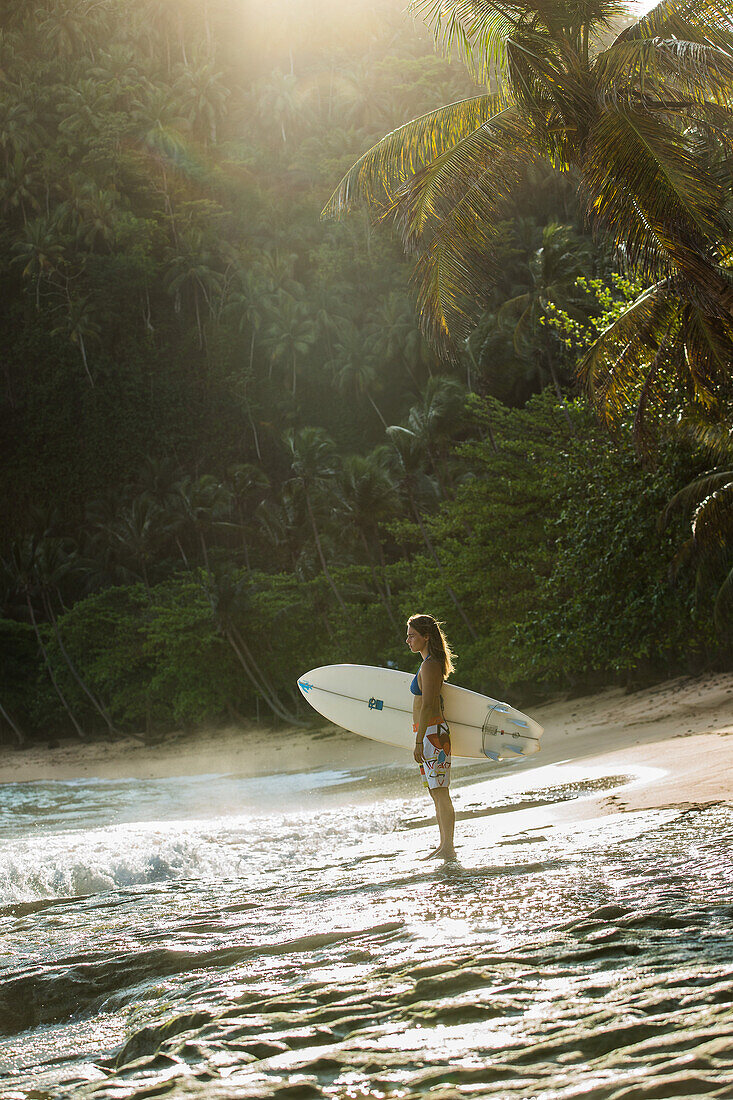 Young female surfer standing with her board on the beach, Sao Tome, Sao Tome and Principe, Africa