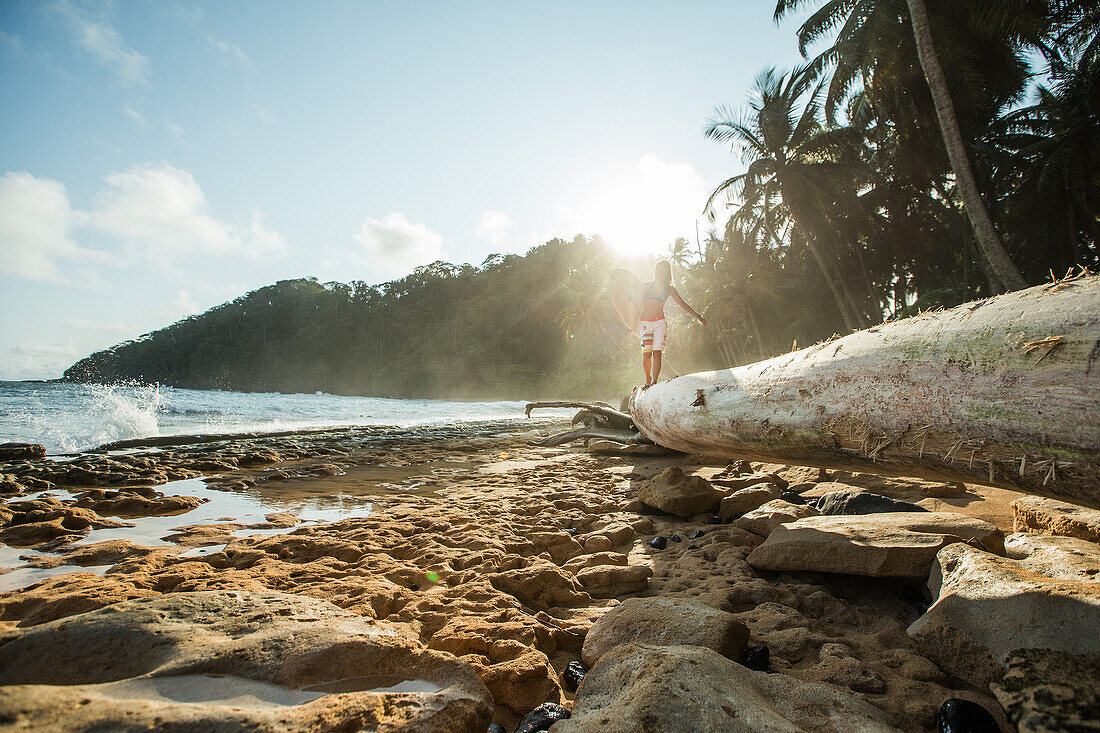 Junge Surferin balanciert über einen Baumstamm am Strand, Sao Tome, Sao Tome und Príncipe, Afrika