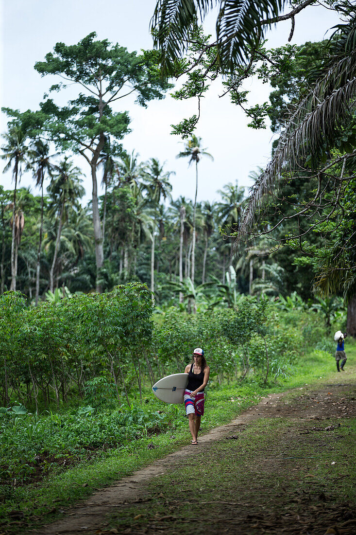 Young female surfer walking on a path through a forest, Sao Tome, Sao Tome and Principe, Africa