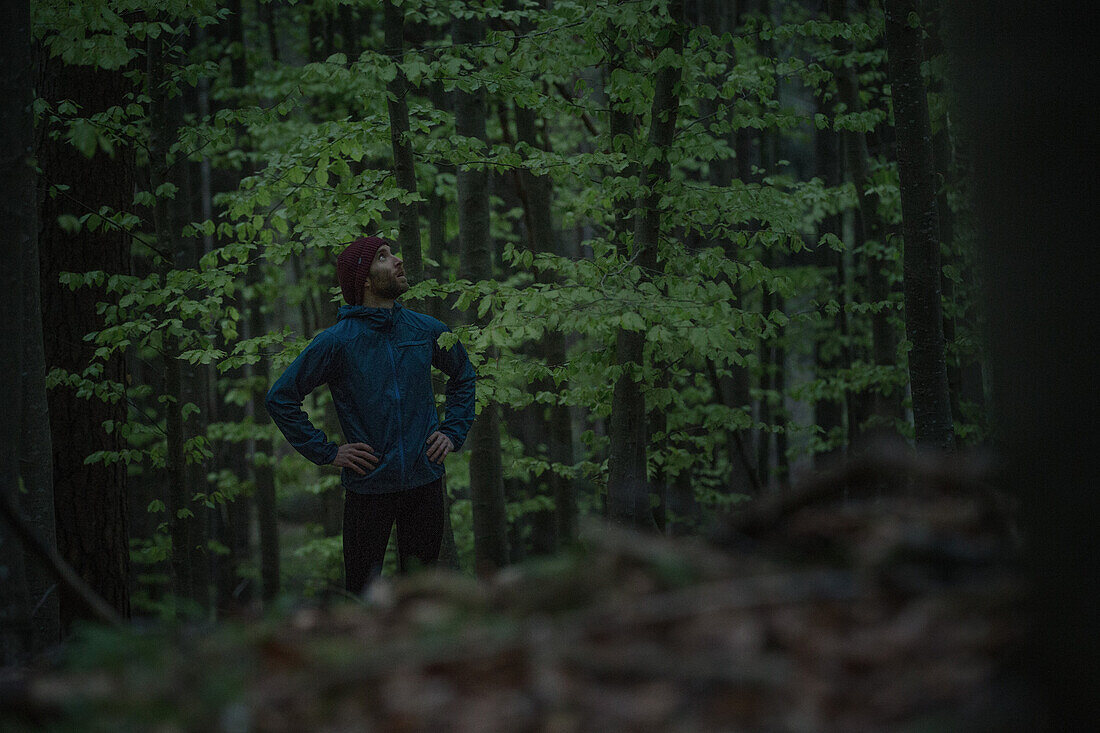 Young male runner having a break and looking at the forest, Allgaeu, Bavaria, Germany