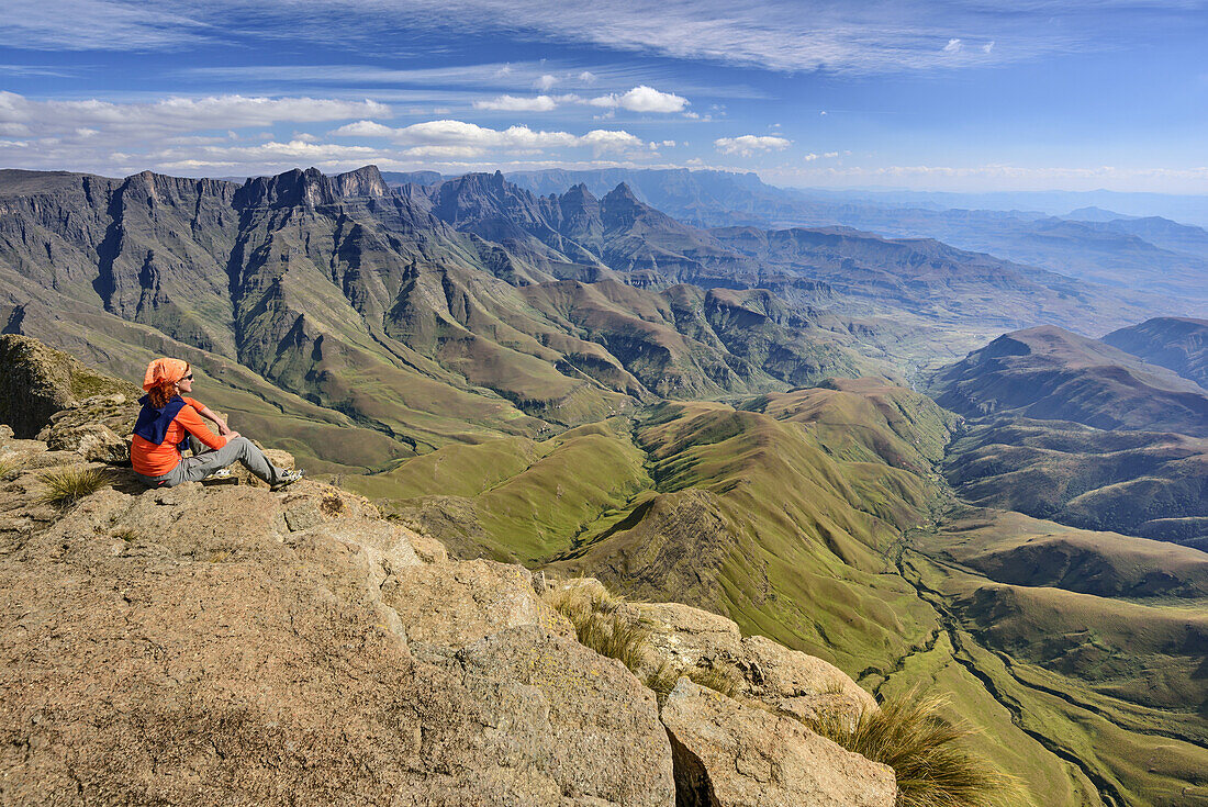 Frau sitzt am Cathedral Peak und blickt auf Mnweni Needles und Amphitheatre, vom Cathedral Peak, Mlambonja Wilderness Area, Drakensberge, uKhahlamba-Drakensberg Park, UNESCO Welterbe Maloti-Drakensberg-Park, KwaZulu-Natal, Südafrika