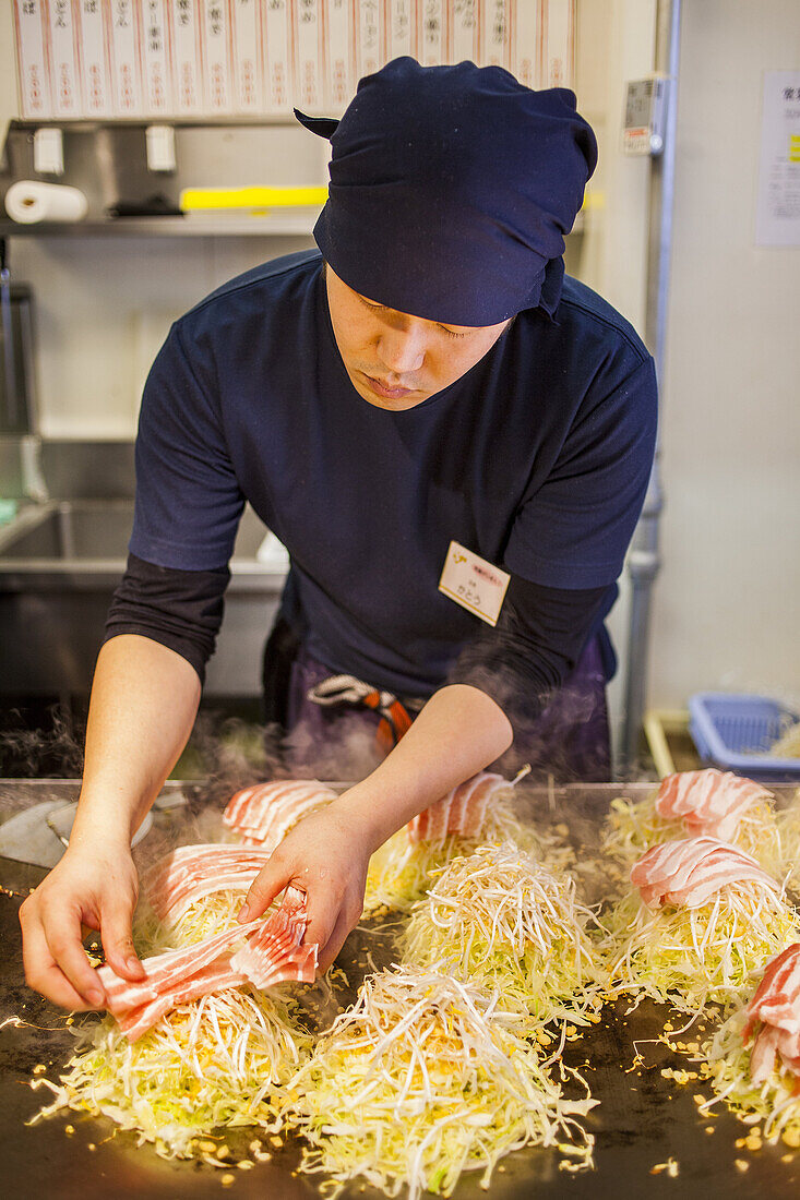 Chef Cooking Okonomiyaki, in a restaurant of Okonomi-mura, Hiroshima, Japan.