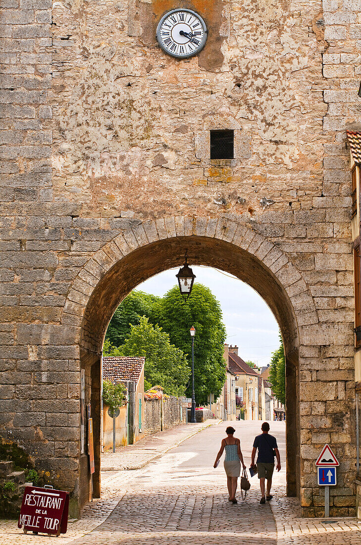 A couple walk out of the old gate in the old part of Noyers sur Serein in Burgundy.
