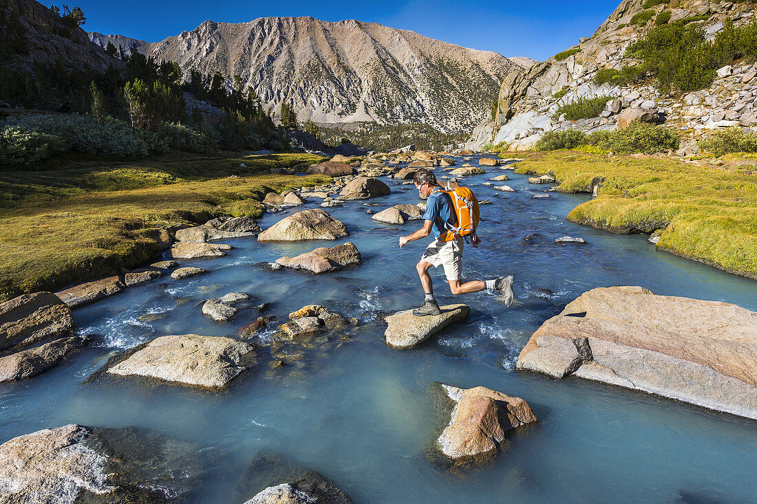 Hiker crossing stream in Sam Mack Meadow, John Muir Wilderness, Sierra Nevada Mountains, California USA.