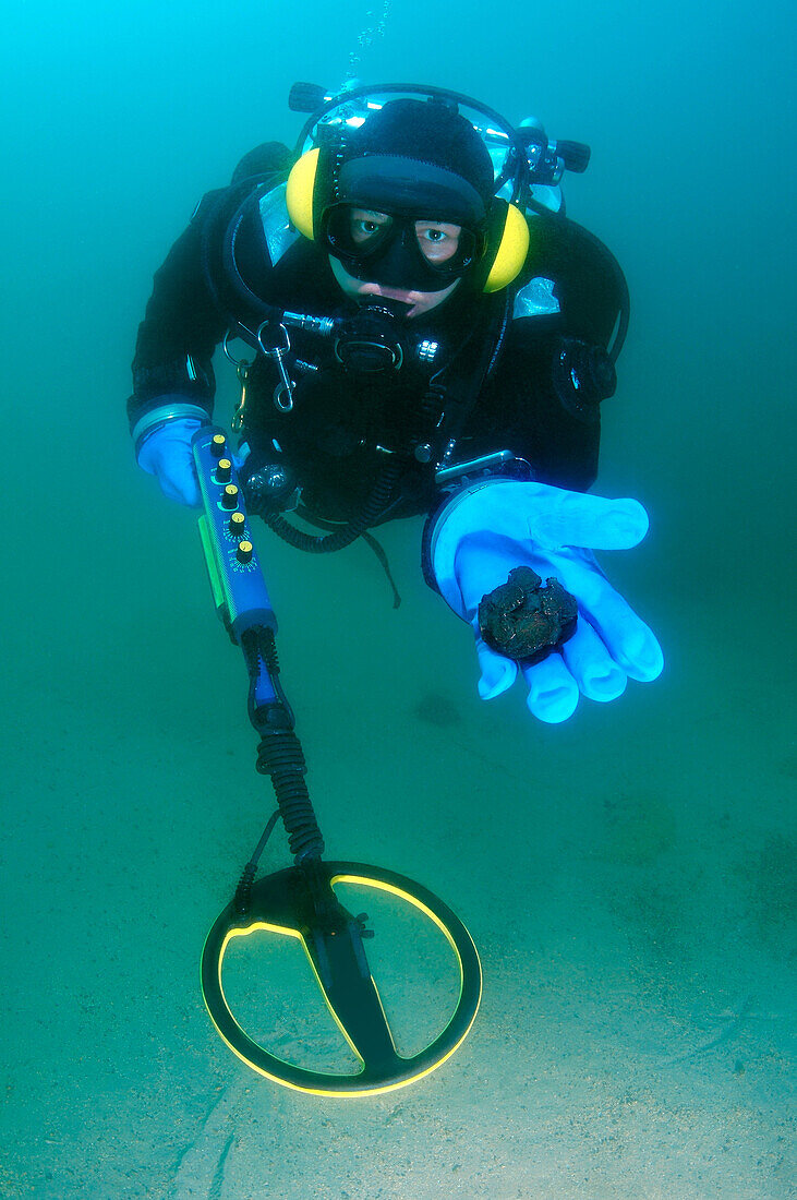 Diver with the metal detector displays the found ancient coins, lake Baikal, Siberia, Russia, Eurasia.