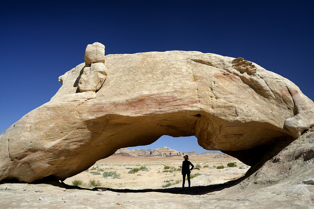 Silhouette of a woman in the shade of a natural rock arch. Jordan, Wadi Rum desert, protected area inscribed on UNESCO World Heritage list. Model Released.