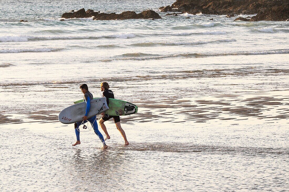 Two surfers running into the sea at Fistral beach in Newquay, Cornwall.