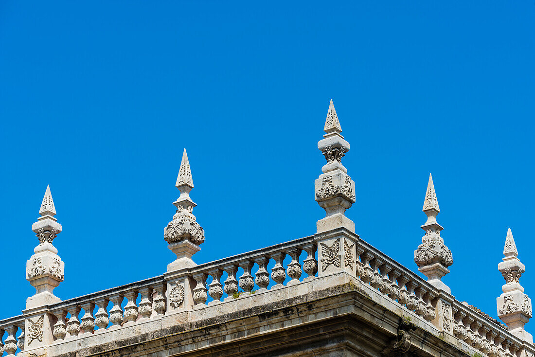 A balcony with stone railings and stone obelisks on a historical building in front of a blue sky, Granada, Andalusia, Spain