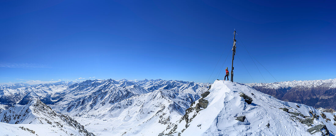 Panorama with woman back-country skiing standing at summit of Hasenoehrl, Brenta group, Presanella group, Ortler group and Oetztal Alps in background, Hasenoehrl, Ortler group, valley of Ultental, National Park Stilfser Joch, South Tyrol, Italy