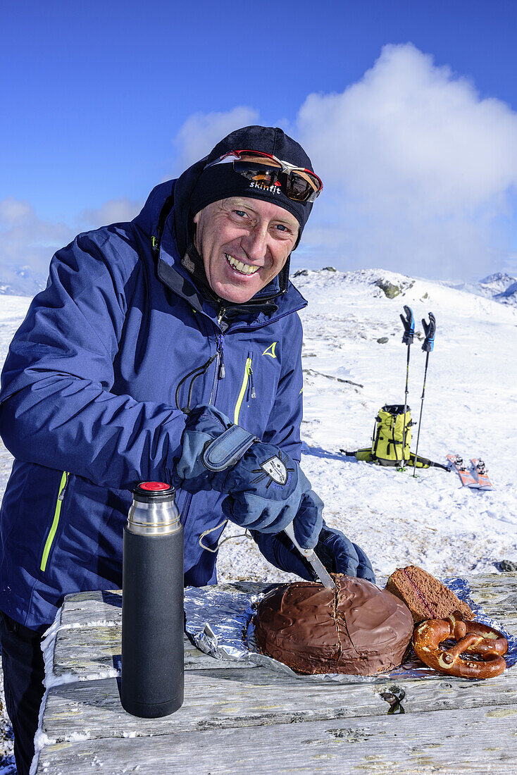 Mann auf Skitour schneidet Kuchen auf, Sonnenjoch, Kitzbüheler Alpen, Tirol, Österreich