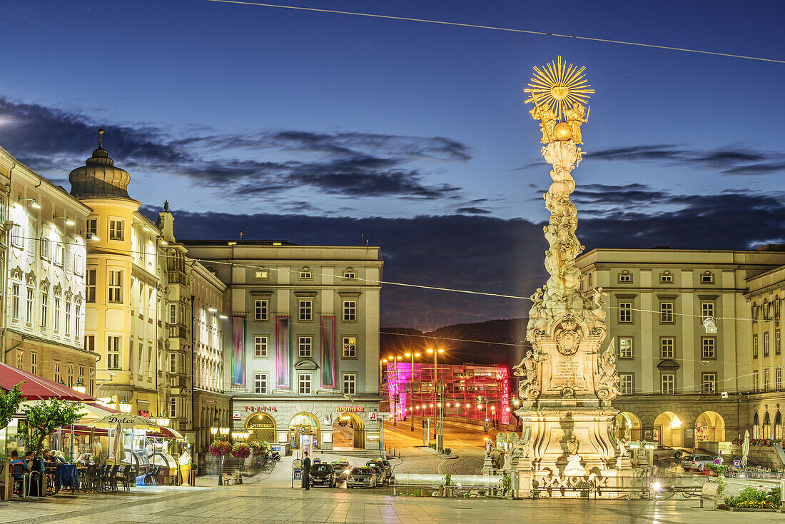 Illuminated city square with pillar Dreifaltigkeitssäule and Ars Electronica Center in background, Linz, Danube Bike Trail, Upper Austria, Austria