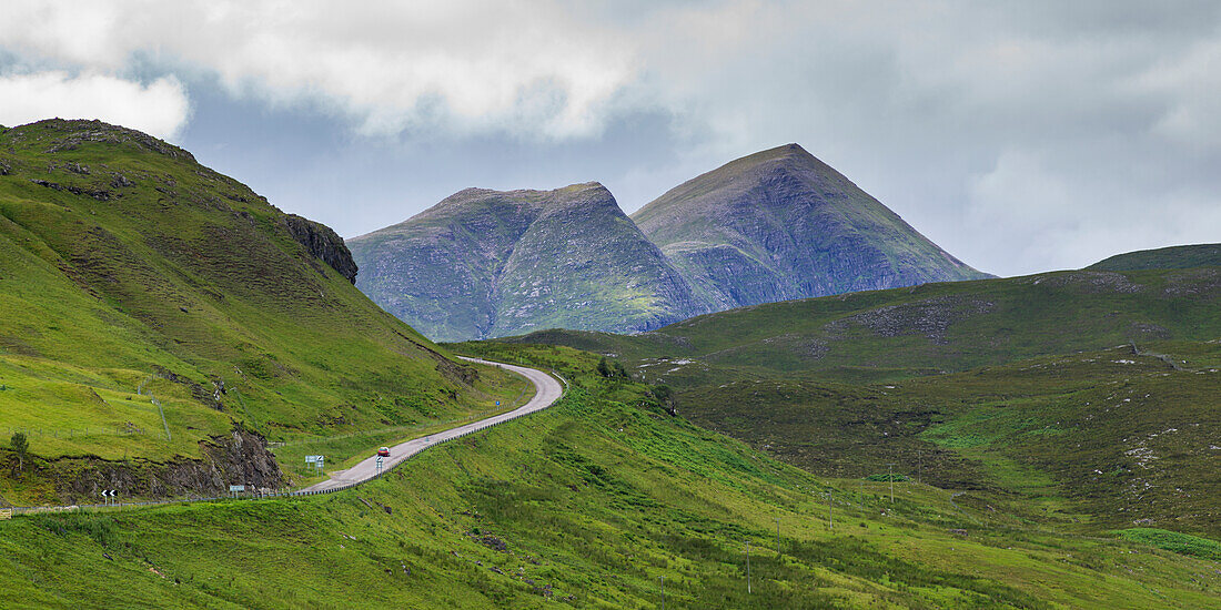 'A road winding through the mountains with two mountain peaks under a cloudy sky in the Highlands; Scotland'