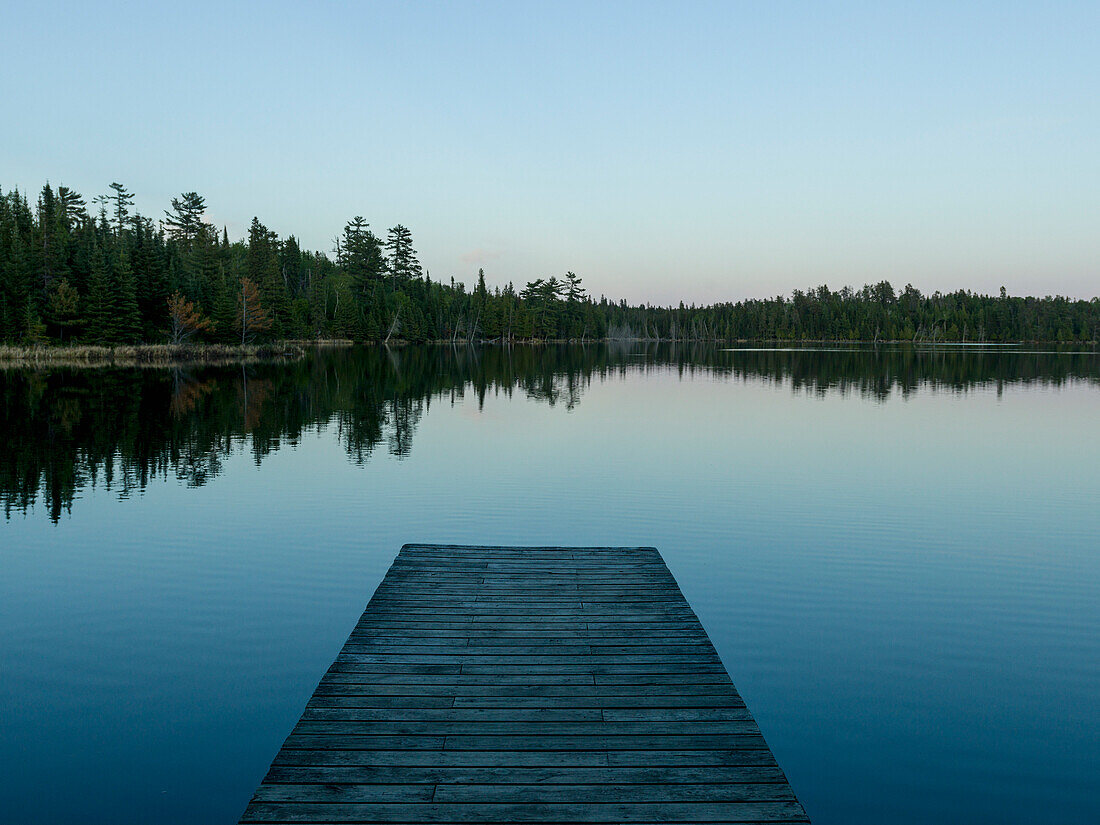 'Wooden dock leading out to a tranquil lake at sunrise; Whiteshell, Manitoba, Canada'