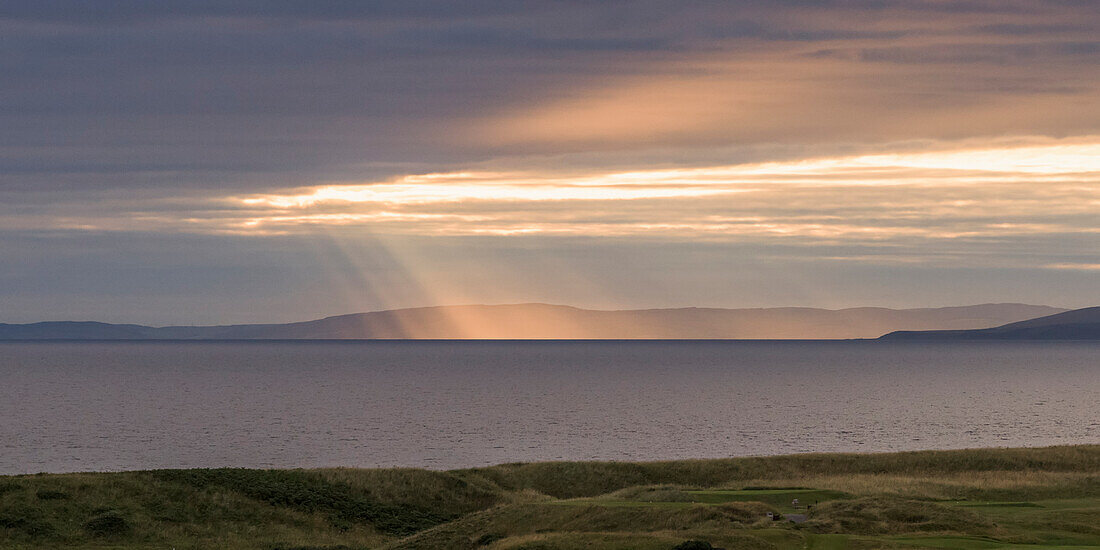 'Sunlight shining through clouds onto the coastline; Turnery, Scotland'