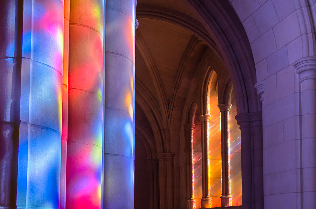 'Light streaming through stained glass windows with colourful light columns along the cathedral nave; Washington, District of Columbia, United States of America'