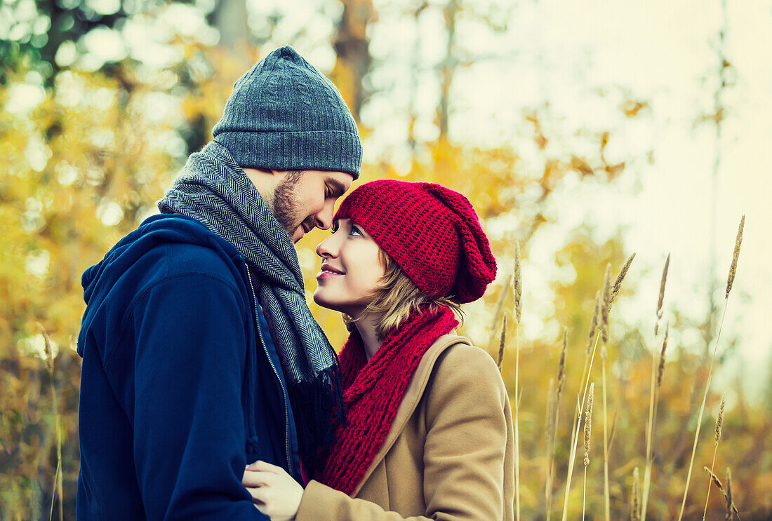 'A young couple looking into each other's eyes and kissing in a city park in autumn; Edmonton, Alberta, Canada'