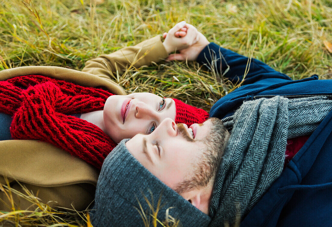 'A young couple laying in the grass and holding hands in a city park in autumn; Edmonton, Alberta, Canada'