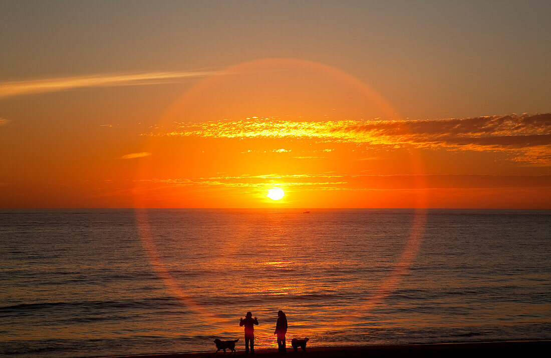 'A halo around the glowing sun as it sets over the ocean and an orange sky; Chiclana de la Frontera, Andalusia, Spain'