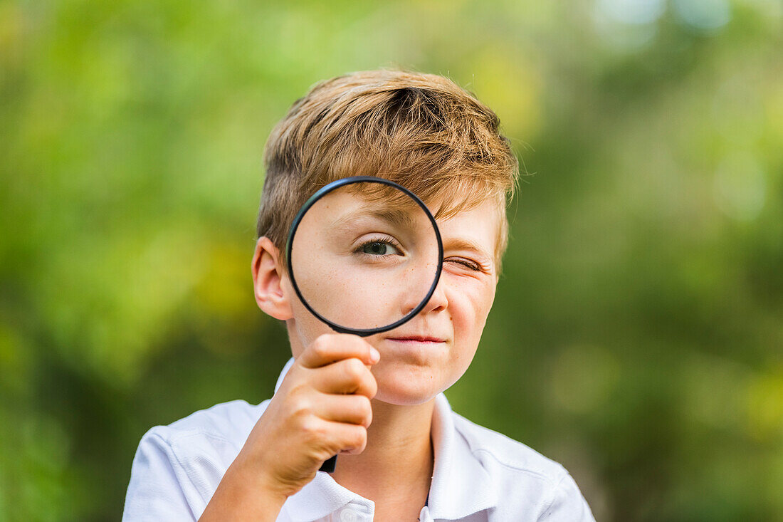 'A young boy using a magnifying glass in a park; Edmonton, Alberta'