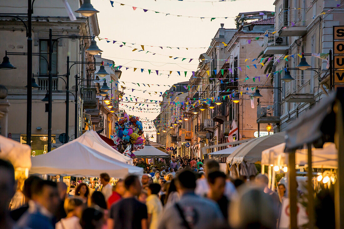 'Tourists walking down a busy street at dusk; Olbia, Sardinia, Italy'