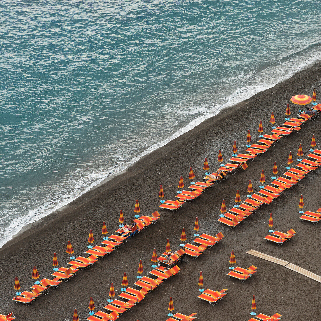 'Rows of colourful lounge chairs and umbrellas on a beach at the water's edge; Positano, Campania, Italy'