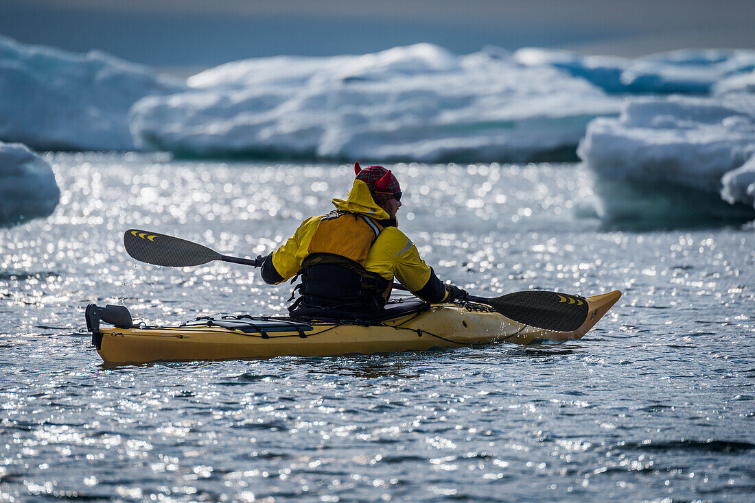 'Backlit kayaker paddling by icebergs in sunlight; Antarctica'