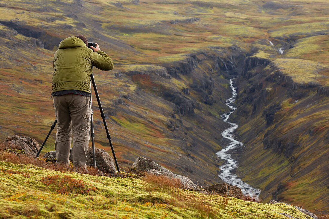 'Man photographing a river valley in Iceland during autumn; Iceland'