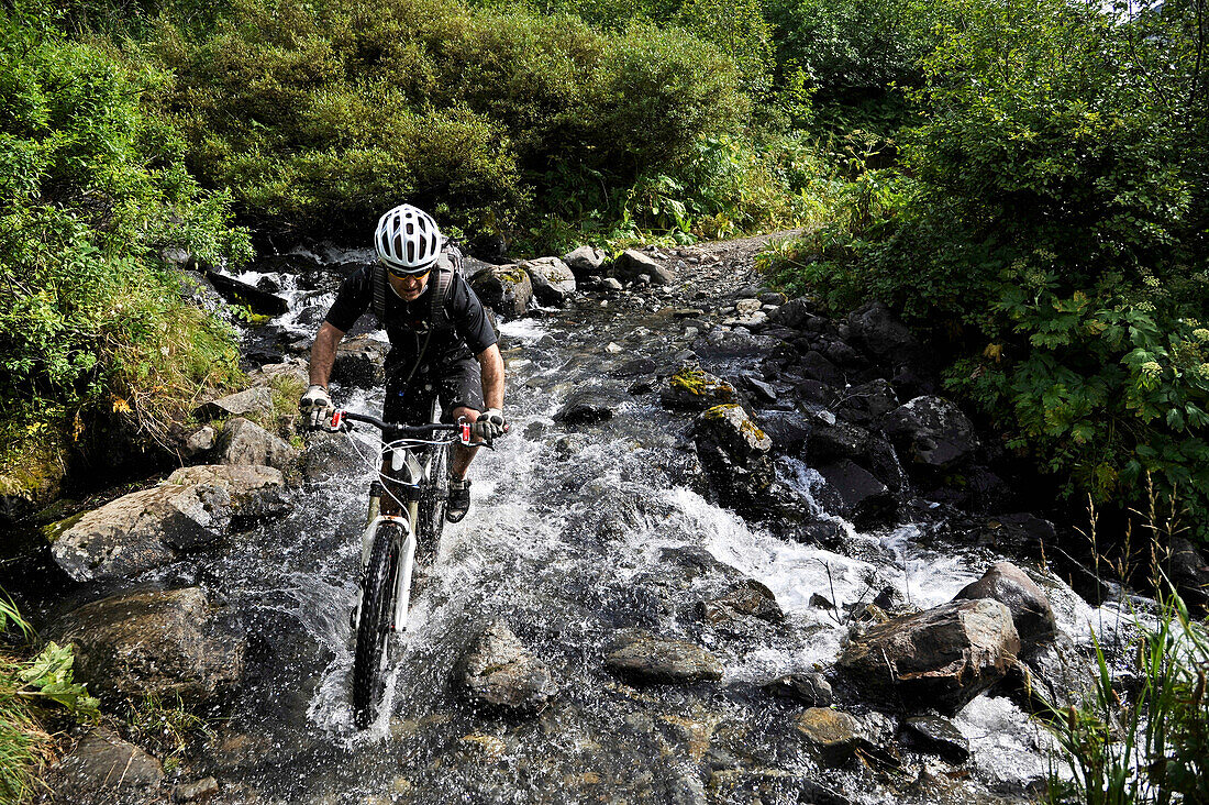 Man rides a full suspension mountain bike across a stream on the Devil's Pass Trail in the Chugach National Forest, Kenai Peninsula, South-central Alaska