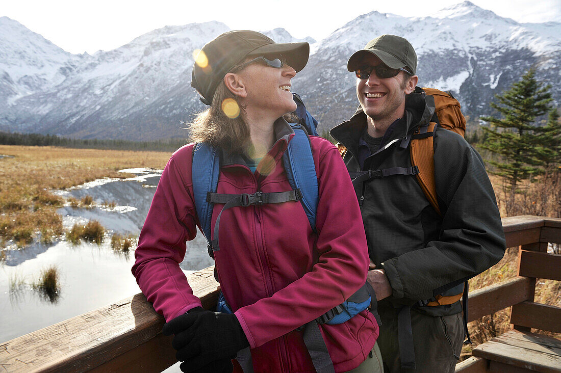 Backpacking couple looks out over the Eagle River Valley and Chugach Mountains from a viewing deck on the Rodak Nature Trail in Chugach State Park near the Eagle River Nature Center in Southcentral Alaska