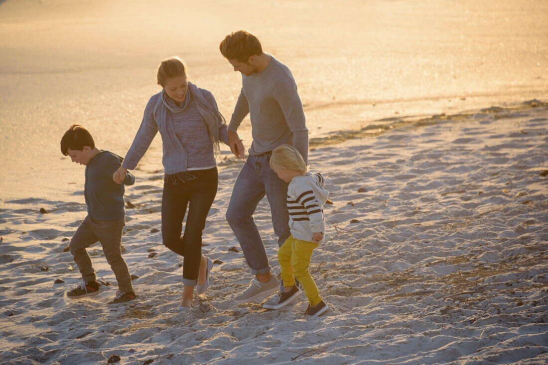 Happy young family walking on the beach at sunset