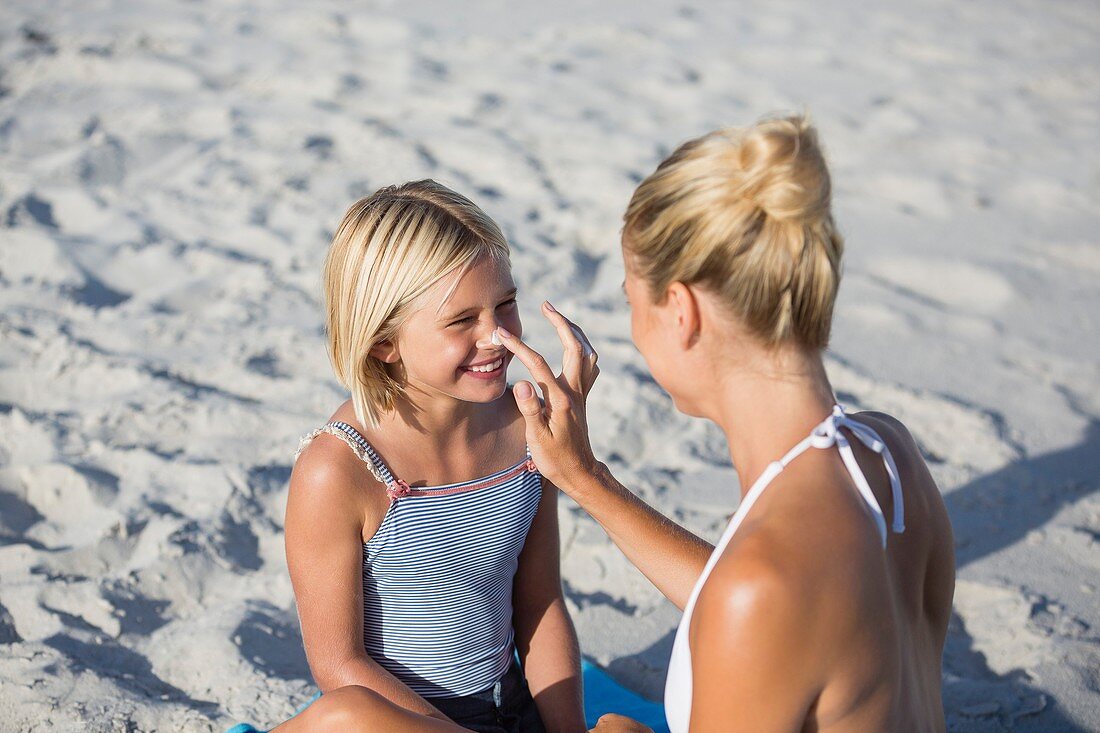 Frau trägt Sonnenschutzmittel auf die Nase ihrer Tochter auf